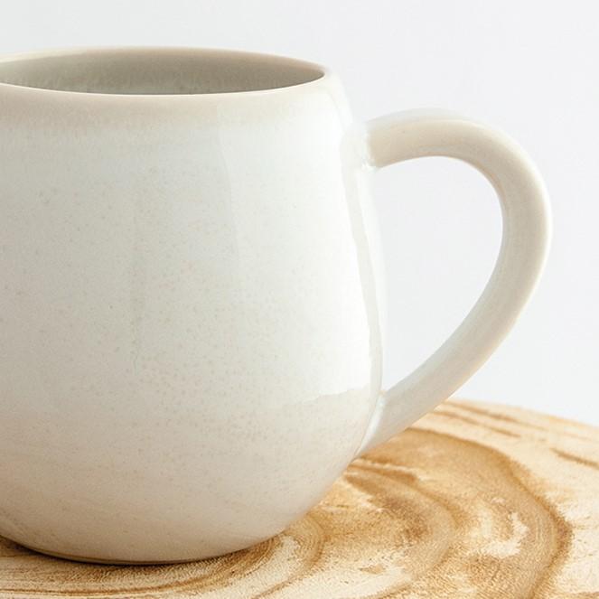 Close up of a Robert Gordon coast white canvas mug coffee cup sitting on a natural wooden round side table