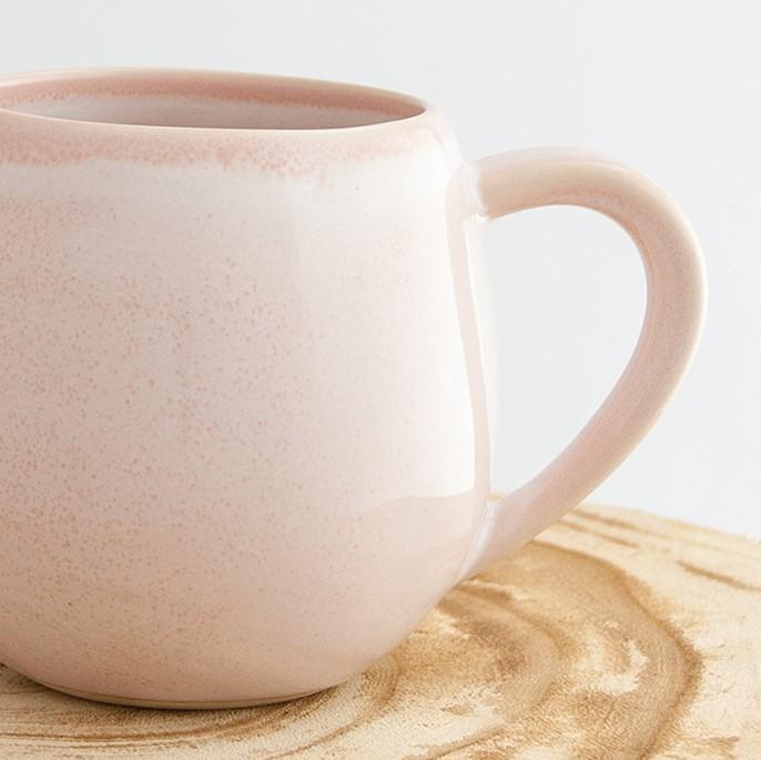 Close up of a Robert Gordon rose quartz pink canvas mug coffee cup sitting on a natural wooden round side table