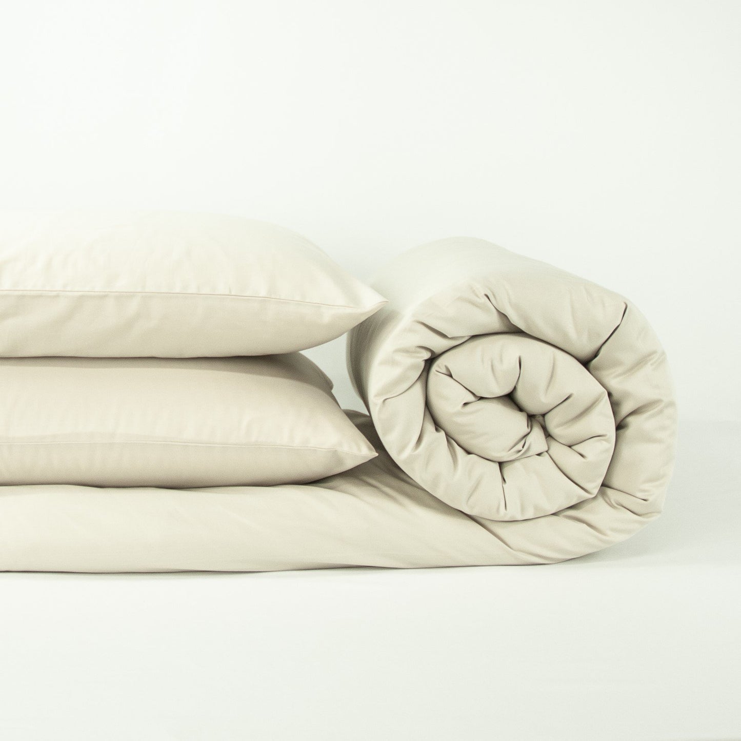 Stack of organic cotton quilt cover set with pillowcases and rolled up quilt cover in egg shell white
