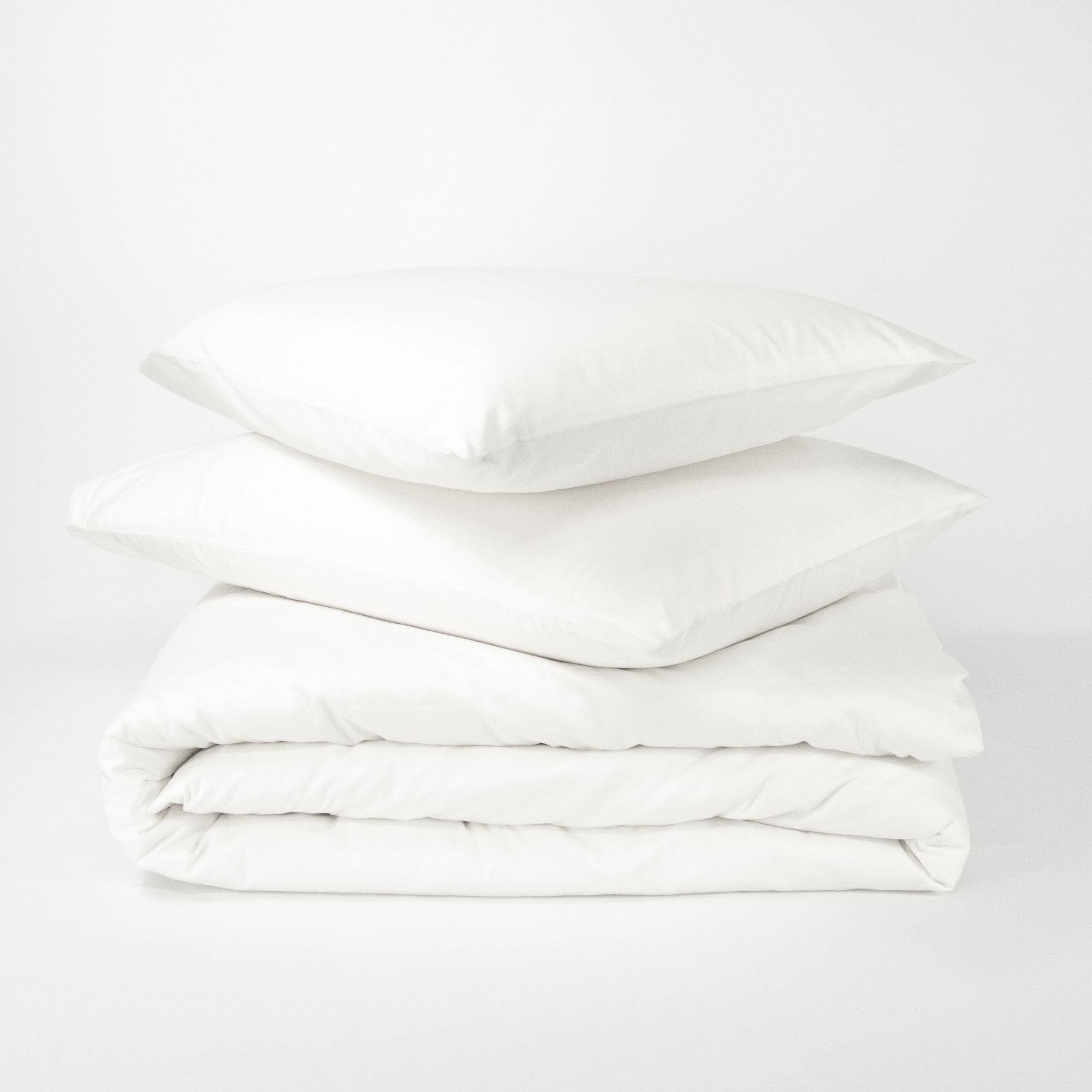 Stack of organic cotton quilt cover set with pillowcases and folded quilt cover in pure white