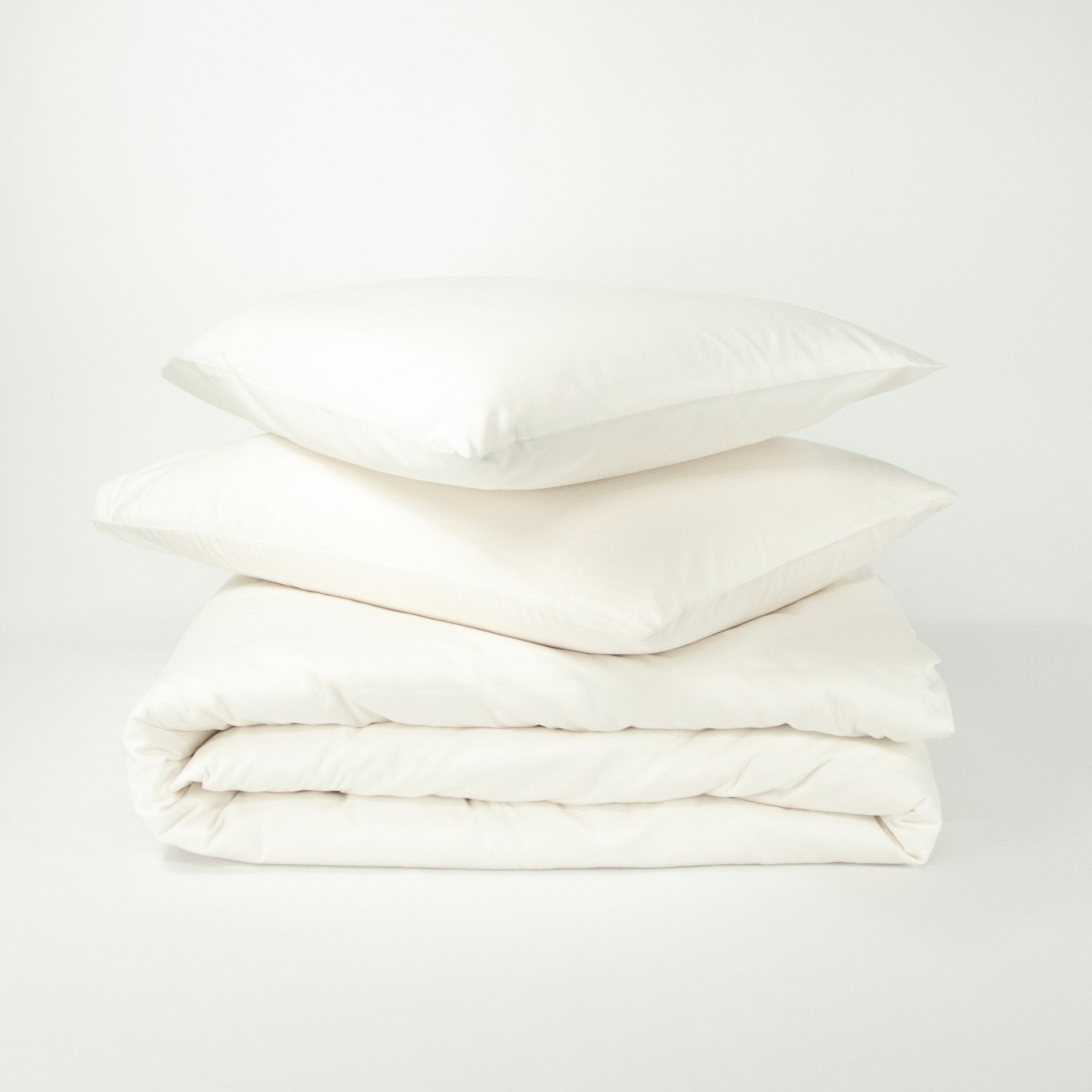 Stack of organic cotton quilt cover set with pillowcases and folded quilt cover in warm white