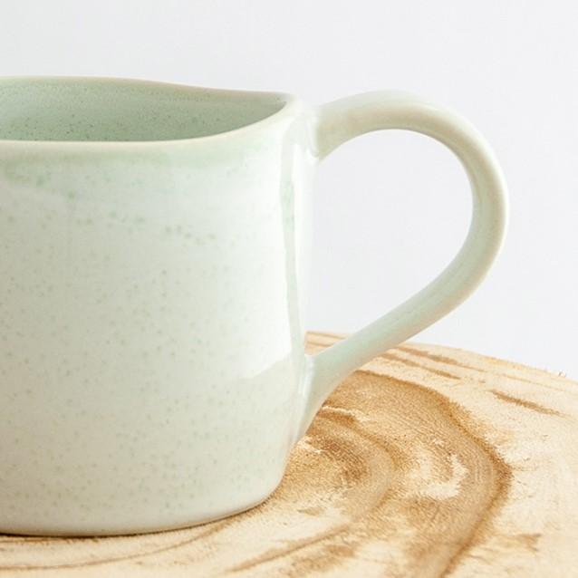 Close up of a Robert Gordon moss green organic mug coffee cup sitting on a natural wooden round side table