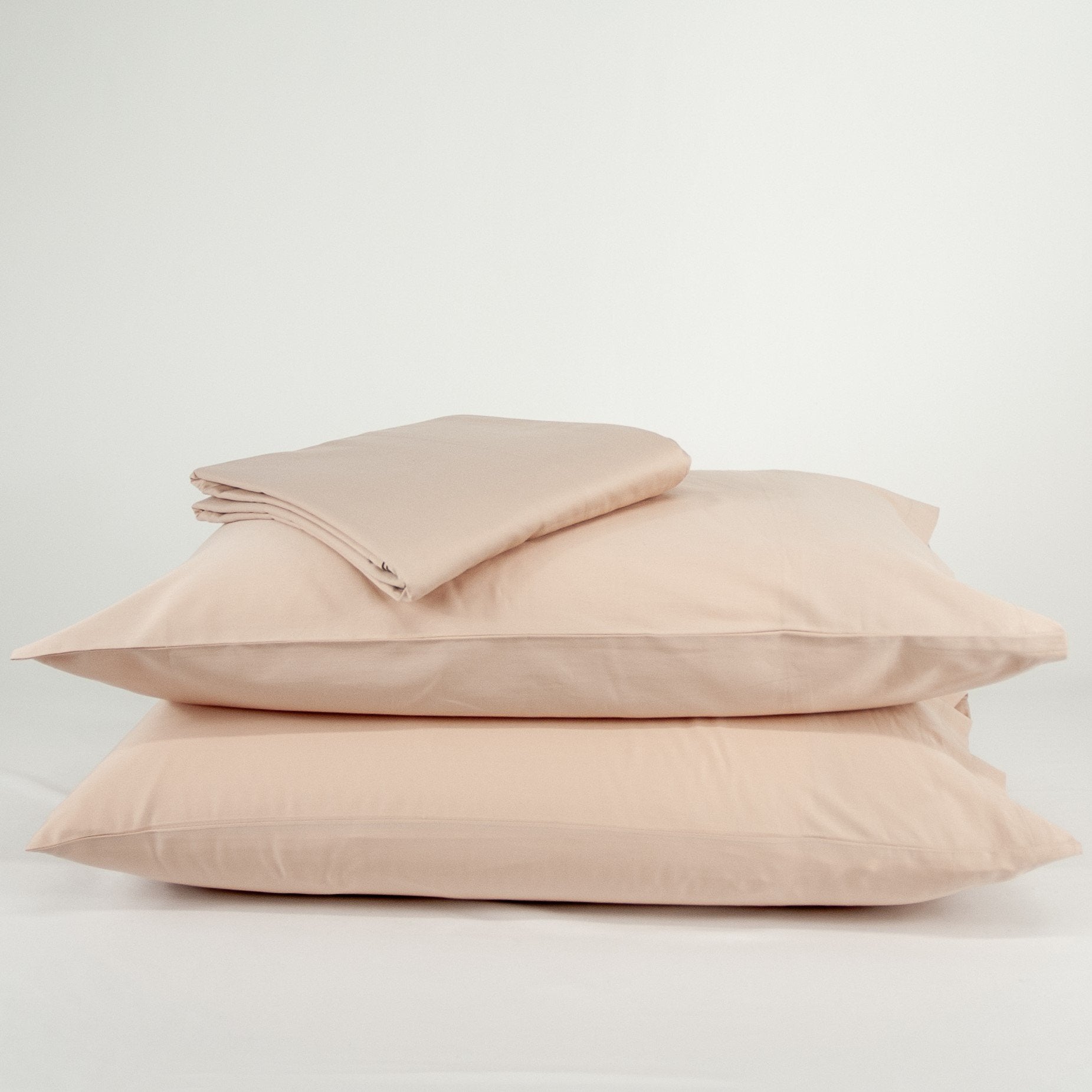 Stacked organic cotton pillowcases and sheets in blush pink