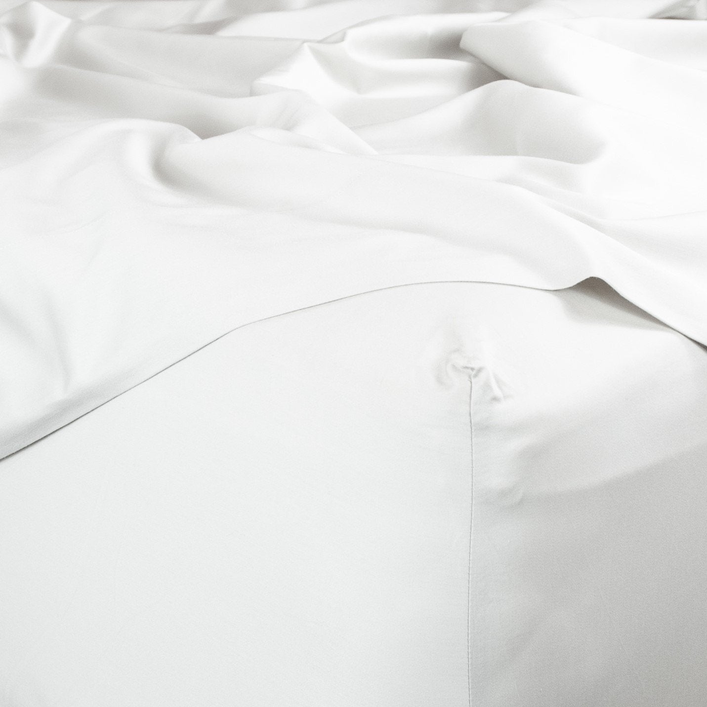 Corner of bed with organic cotton fitted sheet and top sheet in pure white