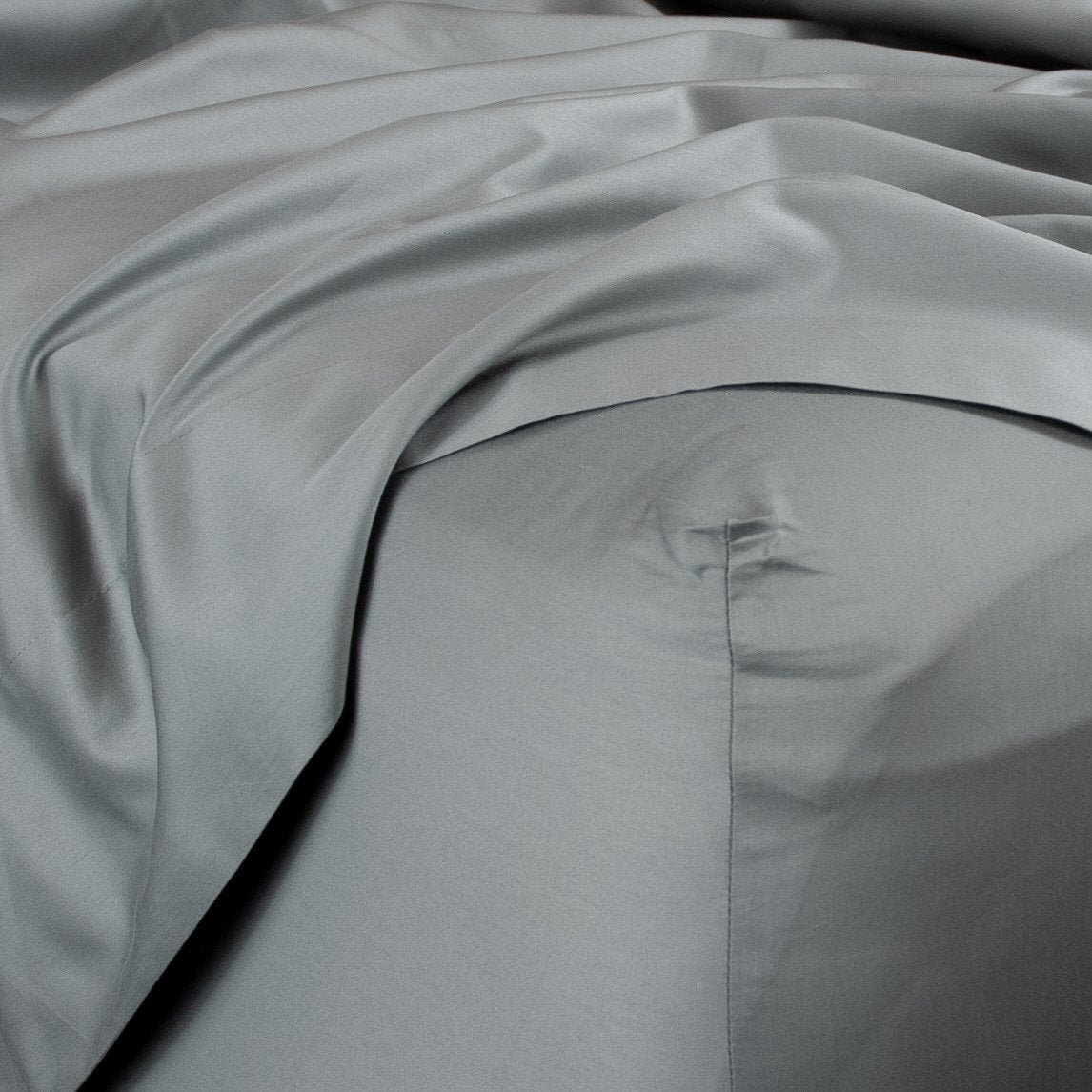 Corner of bed with organic cotton fitted sheet and top sheet in sleet grey