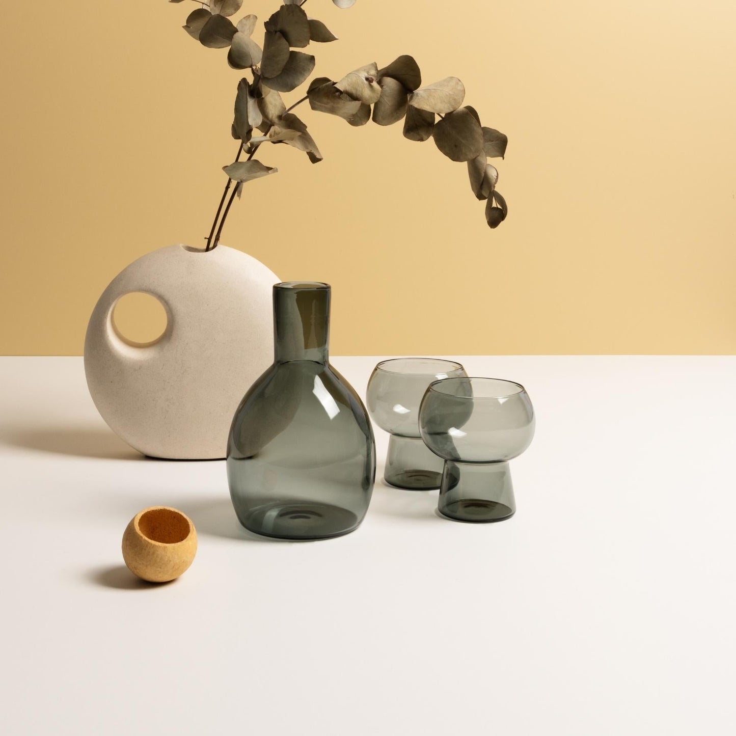 Marnie smoke grey carafe and glasses sitting on white table with round white stoneware vase