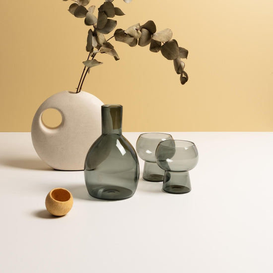 Marnie smoke grey carafe and glasses sitting on white table with round white stoneware vase