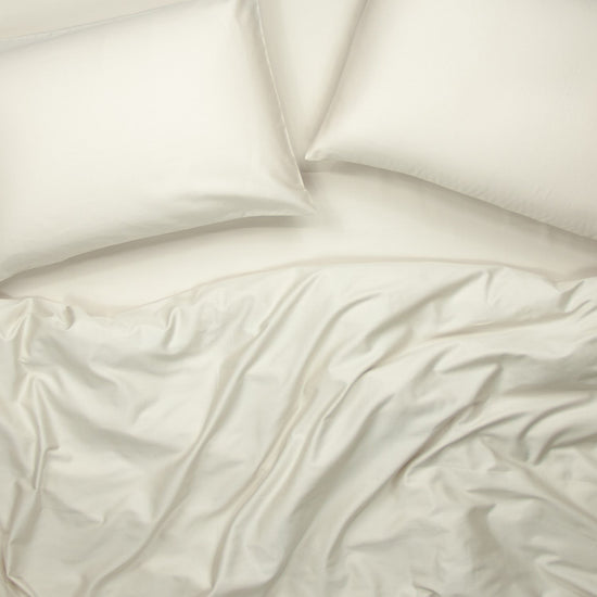 Birds eye view of organic cotton fitted bedding set with pillowcases, fitted sheet and quilt cover in egg shell white