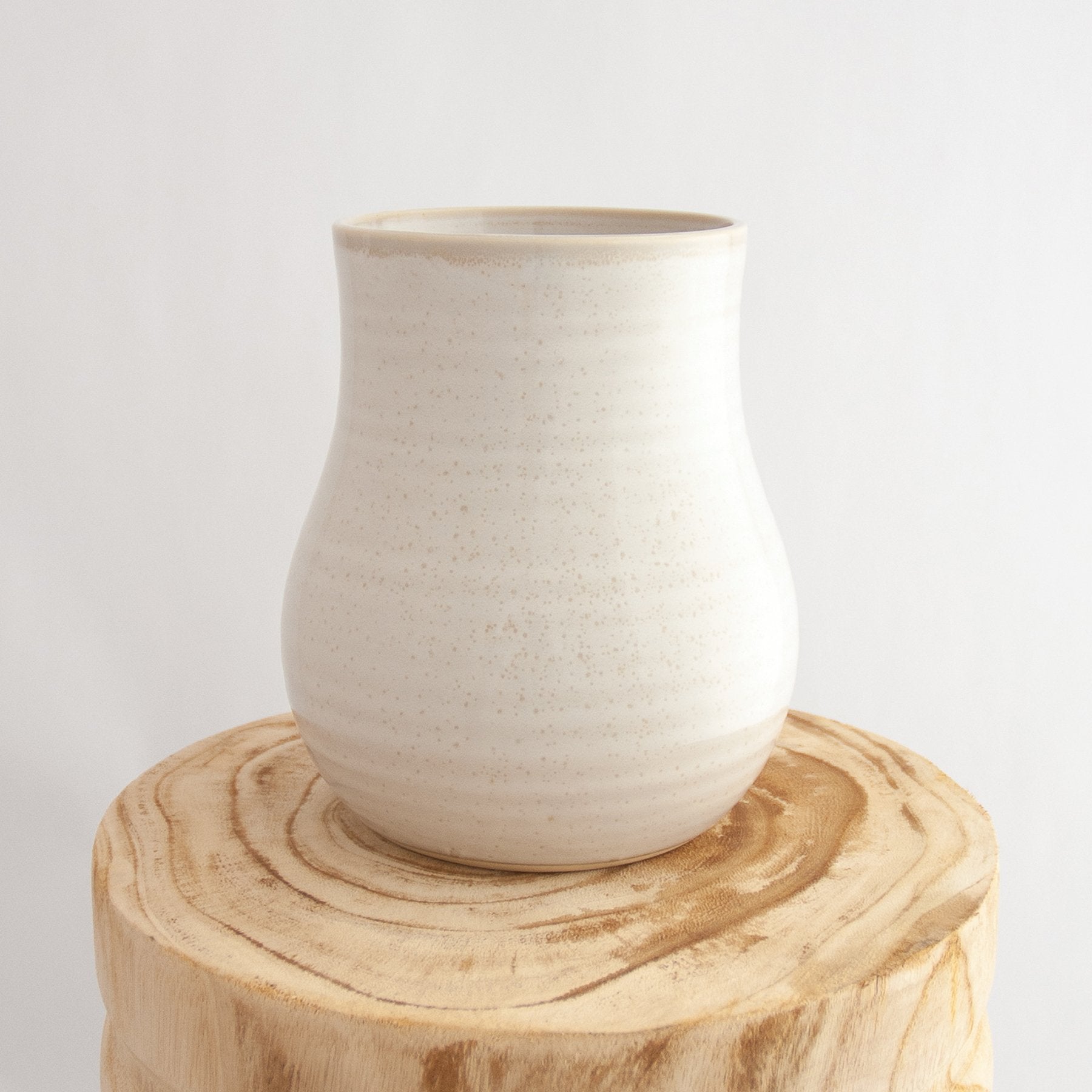 Robert Gordon pottery botanica coast white vase sitting on a natural wooden round side table