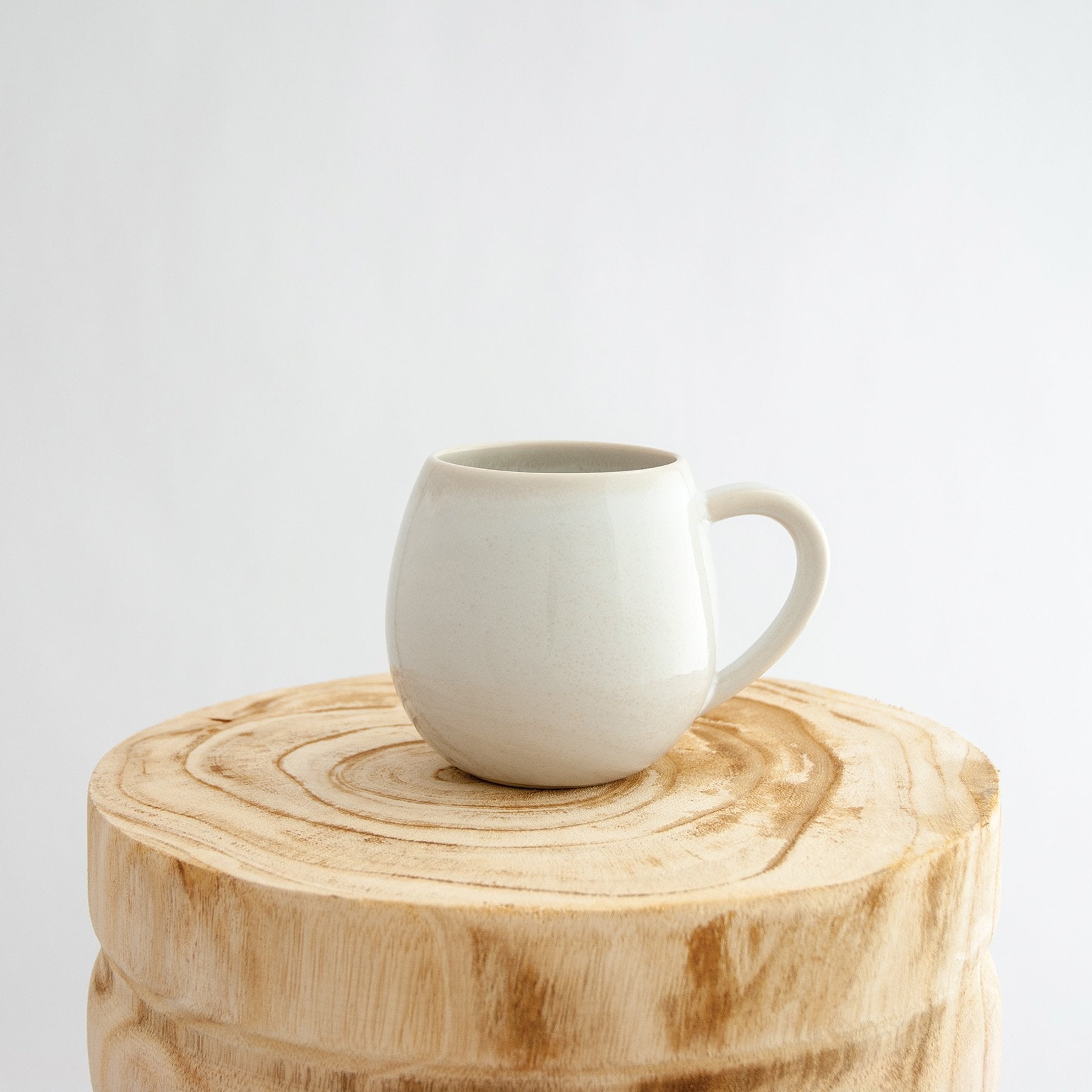 Robert Gordon coast white canvas mug coffee cup sitting on a natural wooden round side table