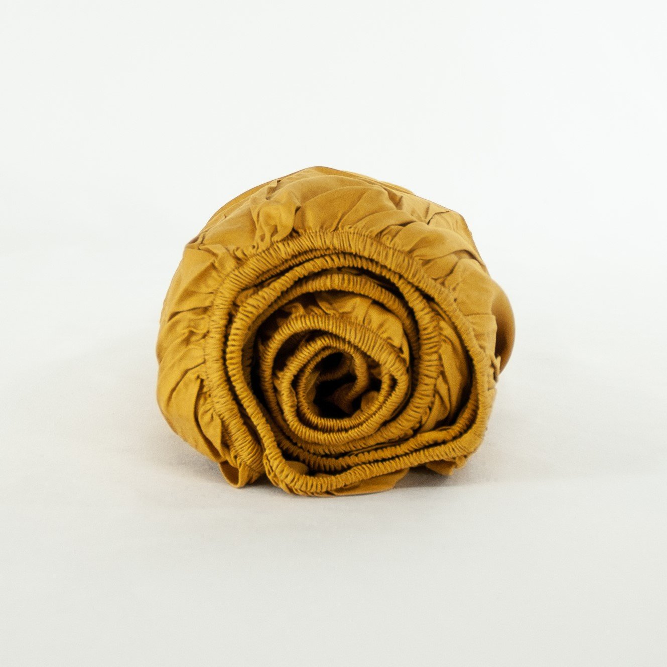 Rolled up organic cotton fitted cot sheet in honey gold