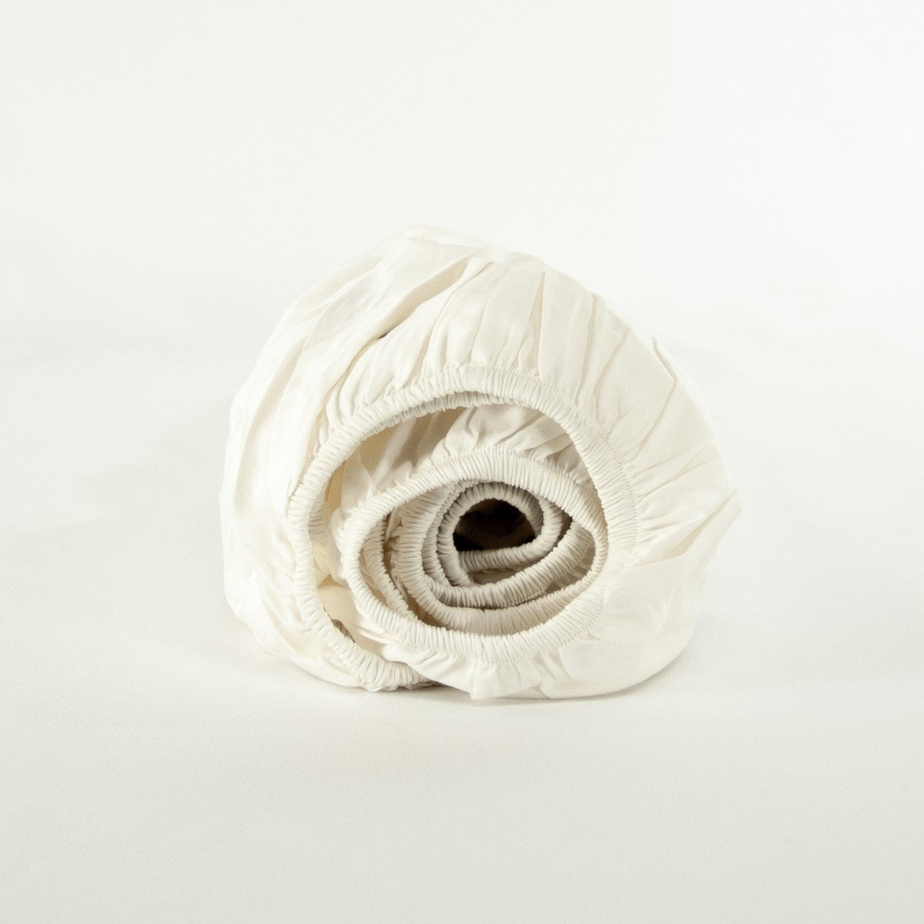 Rolled up organic cotton fitted cot sheet in warm white