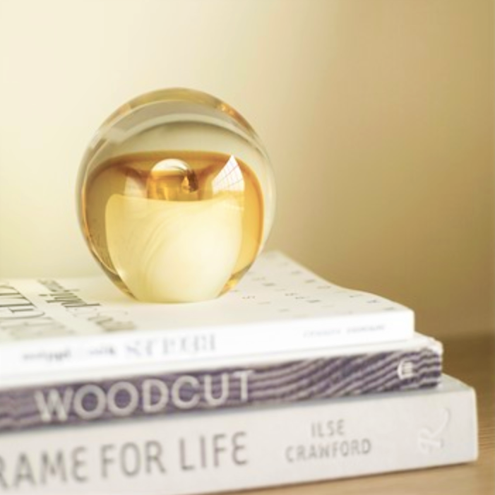 Close up of a Hubsch Interior objet d’art paperweight in honey amber and cream on bookshelf with books