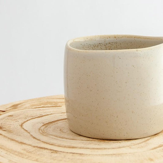 Close up of a Robert Gordon oatmeal cream organic mug coffee cup sitting on a natural wooden round side table